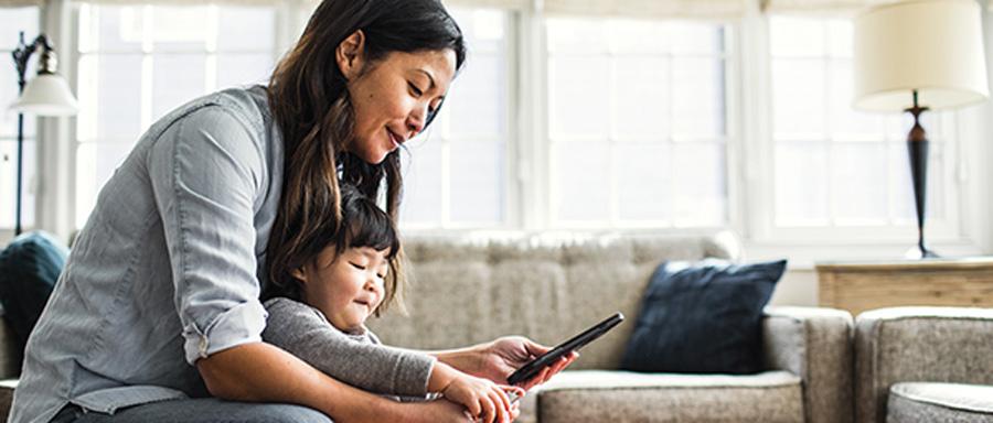A woman holding a toddler while she looks at her phone.