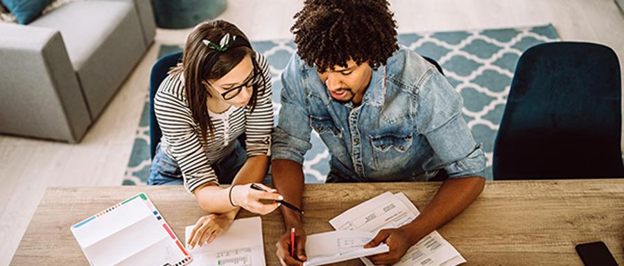 A woman and a man sitting at a table reviewing bills and financial statements.